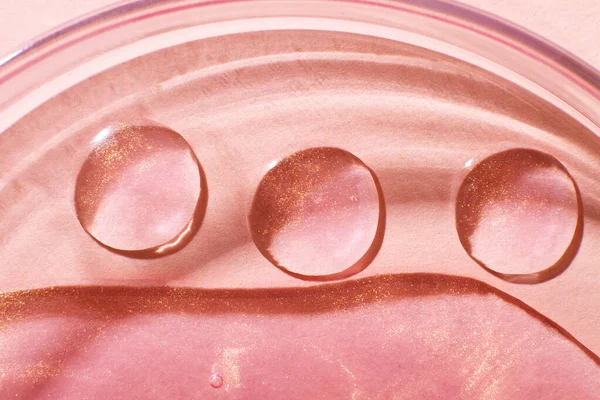 Three drops of liquid rose gold close-up. In a Petri dish. Laboratory research of cosmetics, gel, medicine. Chemistry