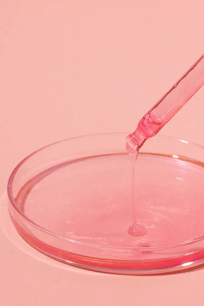 stock image Pipette with dripping pink liquid. Or rose gold. On top of a Petri dish with pink liquid. On a pink background. Laboratory, chemistry, medicine. Cosmetic research. glitter.