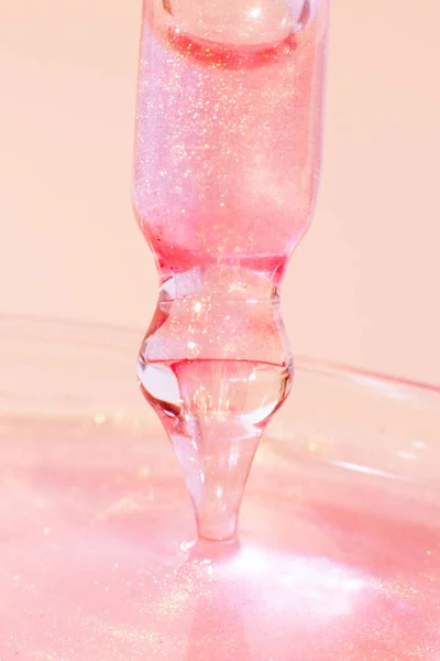 stock image Pipette with dripping pink liquid. Or liquid rose gold. Close-up. On a pink background. Laboratory, chemistry, medicine. Cosmetic research. shine.