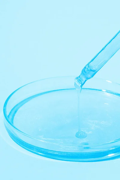 滴着蓝色液体的琵琶 在一个带有蓝色液体的培养皿上 蓝色的背景 实验室 化妆品研究 — 图库照片