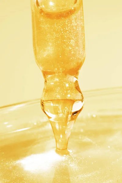 Pipette with dripping yellow liquid. Or liquid gold. Close-up. On a golden background. Laboratory, chemistry, medicine. Cosmetic research. shine.