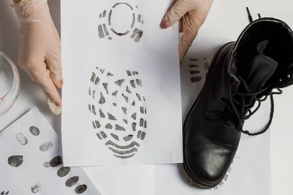 A crime lab technician holds a shoe in his hand. And compares the shoe print with the shoe print. In the crime lab.