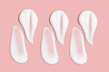 Bir sürü kozmetik kremi. Hafif, pürüzsüz yüzey. Yayılabilir krem dokusu. Sıvı kremsi felçler. Pembe arka planda. Kozmetik arkaplan, afiş.