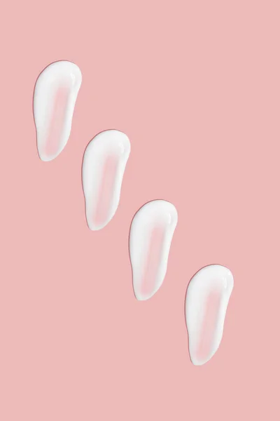 Lots of smears of cosmetic cream. Light, smooth surface. Texture of spreadable cream. Liquid creamy strokes. On a pink background. Cosmetic background, banner.