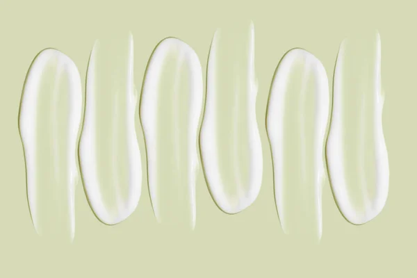 化粧品クリームの多くの笑顔 軽く滑らかな表面 列に並んで 角度で 最上階だ 流れるクリームの質感 液体のクリーミーストローク 緑の背景に 化粧品の背景バナー — ストック写真