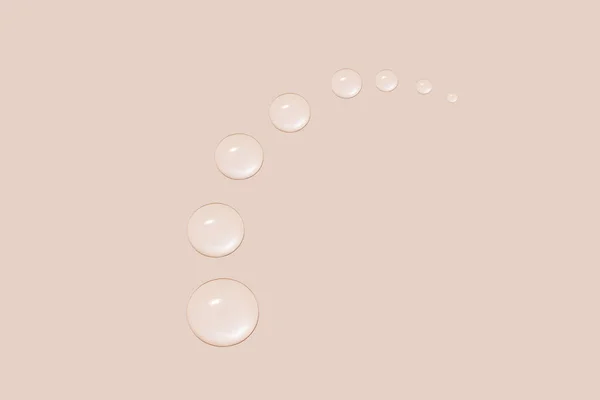 Stock image Drops of transparent gel or water in the shape of a semi-circle, with decreasing size. On a beige background.