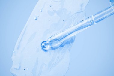 Düşürücüden akan şeffaf kozmetik jel ve arka plana bulaşmış. Mavi arka planda. Hyaluronik asit, tonik, tonik, jöle, krem. Kozmetik.