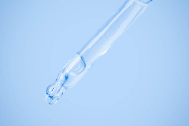 Düşürücüden şeffaf kozmetik jel akıyor. Mavi arka planda. Hyaluronik asit, tonik, tonik, jöle, krem. Kozmetik.