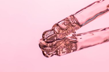 Yakın planda şeffaf köpüklü jel döküldü. Pipetten sızıyor. Pembe tonlarda