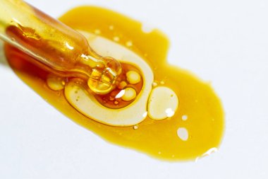 Beyaz arka planda kabarcıklar ve çizgiler olan sarı sıvı pipetten çıkıyor.. 