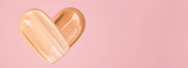 The foundation is smeared in the shape of a heart on a light pink background. Tone cream
