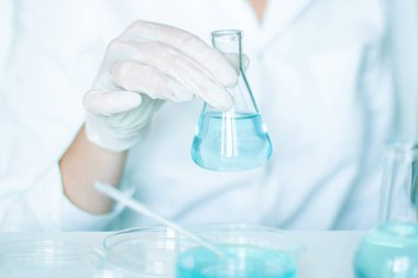 Laboratuvar işleri, asistanlar prosedürleri uygular. Eldiven giyiyordu, beyaz giymişti. Cam aletler kullanarak. Açık mavi sıvı değiştirildi.