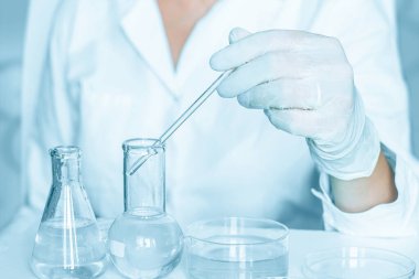 Laboratuvarda: Laboratuvar ortamında eylemleri dikkatle gerçekleştirmede yardımcı olun. Laboratuvar önlüğü giyiyordu. Cam teçhizatı kullanılıyor. Mavi bir labaratuvarda. Şeffaf sıvıyla araştırma yapıyor..