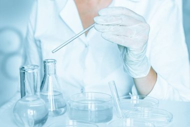 Laboratuvarda: Laboratuvar ortamında eylemleri dikkatle gerçekleştirmede yardımcı olun. Laboratuvar önlüğü giyiyordu. Cam enstrümanlar kullanılıyor. Mavi laboratuvar içeriği. Şeffaf sıvıyla araştırma yapıyor..