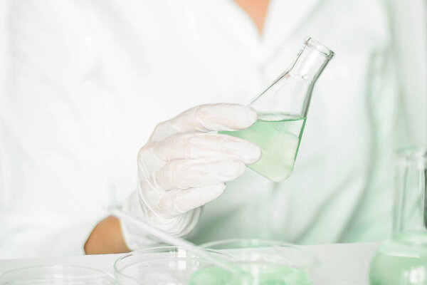 Scientific scene: Assistant performs tasks within the laboratory. Lab coat attire. Green palette. Glass tools utilized. Engaged in plant research in the green laboratory.