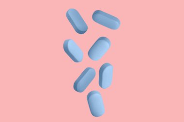 Mavi kapsüller, haplar ve tabletler havada uçuşuyor. Pembe bir arka planda.