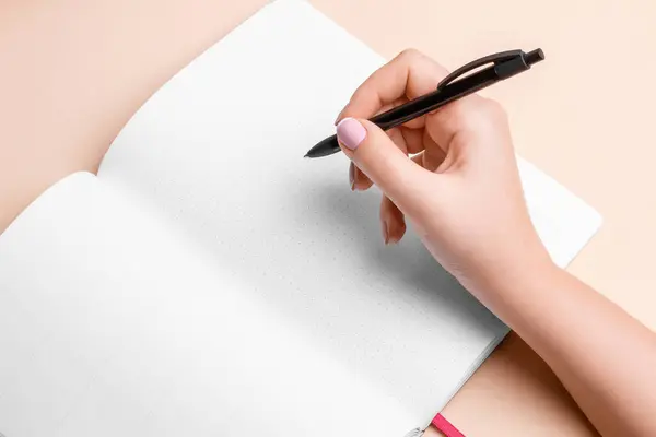 A woman\'s hand holds a pen and is about to write in a notepad