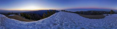 Arkasında güzel bir günbatımı olan karlı bir dağın panoramik görüntüsü. Gökyüzü turuncu ve mor renklerin karışımıdır. Huzurlu ve huzurlu bir atmosfer yaratır.