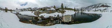 Pacific Crest Patikası. Karlı bir manzaranın panoramik bir görüntüsü ve içinden bir nehir akıyor. Sahne huzurlu ve sakin, karla kaplı zemin ve sakin su bir huzur hissi yaratıyor.