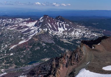 Pacific Crest Patikası. Tepesinde kar ve altında göl olan bir dağ sırası. Gökyüzü mavi ve dağlar uzakta.