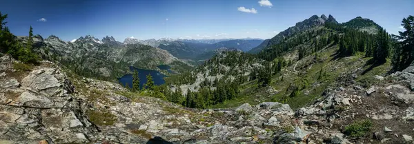 stock image Pacific Crest Trail. A panoramic view of a mountain range with a lake in the foreground. The sky is clear and the mountains are covered in snow. The scene is peaceful and serene, with the mountains