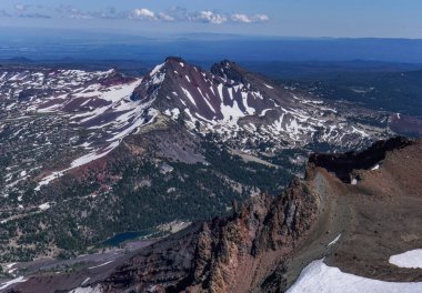 Pacific Crest Patikası. Tepesinde kar ve altında göl olan bir dağ sırası. Gökyüzü mavi ve dağlar uzakta.