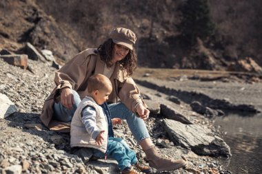 Küçük bir çocuğu olan güzel bir anne göl kenarında ve parkta bir oğlan yürür. Gülümserler, sarılırlar ve doğaya hayran kalırlar..