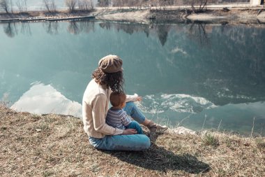 Küçük bir çocuğu olan güzel bir anne göl kenarında ve parkta bir oğlan yürür. Gülümserler, sarılırlar ve doğaya hayran kalırlar..