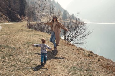 Küçük bir çocuğu olan güzel bir anne göl kenarında ve parkta bir oğlan yürür. Gülümserler, sarılırlar ve doğaya hayran kalırlar..