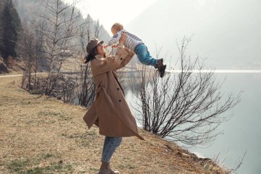 Küçük bir çocuğu olan güzel bir anne göl kenarında ve parkta bir oğlan yürür. Gülümserler, sarılırlar ve doğaya hayran kalırlar..