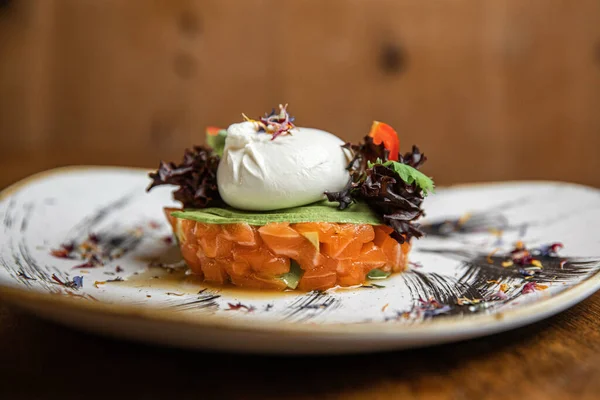 Raw salmon, avocado purple onion salad served in culinary ring on black plate. Wooden background