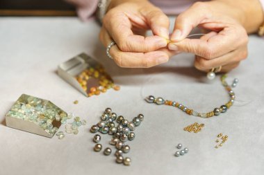Bir kadın değerli taşlardan bir kolye topluyor. Yukarıdan bak. El yapımı. Mücevher sanatı.