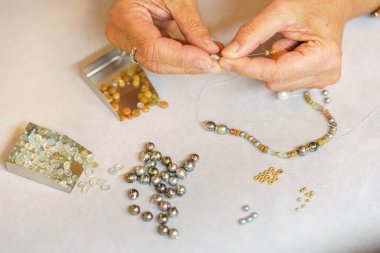 Bir kadın değerli taşlardan bir kolye topluyor. Yukarıdan bak. El yapımı. Mücevher sanatı.
