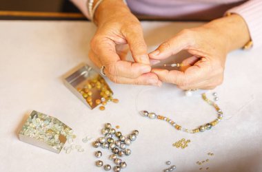 Bir kadın değerli taşlardan bir kolye topluyor. Yukarıdan bak. El yapımı. Mücevher sanatı.