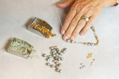 Bir kadın değerli taşlardan bir kolye topluyor. Yukarıdan bak. El yapımı. Mücevher sanatı.