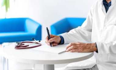 Hastanede steteskopla reçete yazan beyaz önlüklü bir doktor. Doktorlar beyaz bir arkaplan üzerinde elleri yakın çekim.