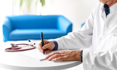 Hastanede steteskopla reçete yazan beyaz önlüklü bir doktor. Doktorlar beyaz bir arkaplan üzerinde elleri yakın çekim.