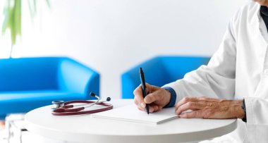 Hastanede steteskopla reçete yazan beyaz önlüklü bir doktor. Doktorun elleri beyaz arka planda..