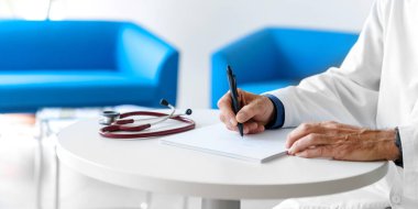 Hastanede steteskopla reçete yazan beyaz önlüklü bir doktor. Doktorun elleri beyaz arka planda..