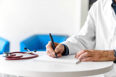 Hastanede steteskopla reçete yazan beyaz önlüklü bir doktor. Doktorun elleri beyaz arka planda..