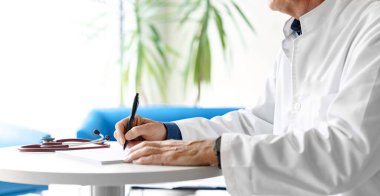 Hastanede steteskopla reçete yazan beyaz önlüklü bir doktor. Doktorun elleri beyaz arka planda..