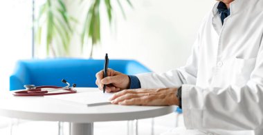 Hastanede steteskopla reçete yazan beyaz önlüklü bir doktor. Doktorun elleri beyaz arka planda..