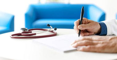 Hastanede steteskopla reçete yazan beyaz önlüklü bir doktor. Doktorun elleri beyaz arka planda..