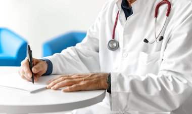 Hastanede steteskopla reçete yazan beyaz önlüklü bir doktor. Doktorun elleri beyaz arka planda..