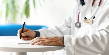 Hastanede steteskopla reçete yazan beyaz önlüklü bir doktor. Doktorun elleri beyaz arka planda..