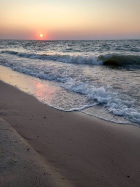 Denizin üzerinde güzel bir günbatımı ön planda kumlu bir plaj, arka planda denizin sakin bir suyu..