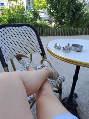 Bir kadın bacağının dikey görüntüsü ve masanın üzerinde beyaz ayakkabılar.