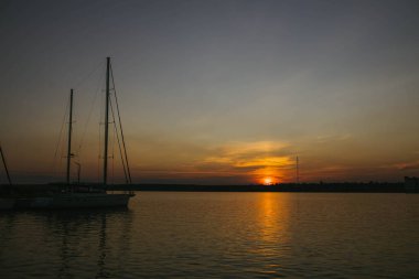 Güney Ukrayna, Mykolaiv - 21 Ağustos 2021: Nehir kıyısında gün batımı, güneş su yüzeyine yansıyor. Kumsaldaki yat ve tekneler, dinlenen insanlar, huzurlu şehirde sakin bir atmosfer. 