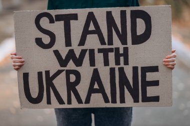 Ukraynalı kız savaşı protesto ediyor, pankart taşıyor, yazılı mesaj yazıyor Ukrayna 'nın yanında dur, sokak geçmişi. Kriz, barış, Rus saldırı konsepti. Savaş karşıtı gösteri..