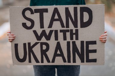 Ukraynalı kız savaşı protesto ediyor, pankart taşıyor, yazılı mesaj yazıyor Ukrayna 'nın yanında dur, sokak geçmişi. Kriz, barış, Rus saldırı konsepti. Savaş karşıtı gösteri..